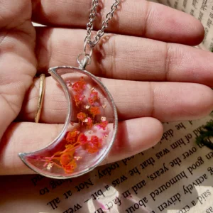 A handcrafted crescent moon-shaped pendant made of clear resin, with a real, small flower suspended inside.