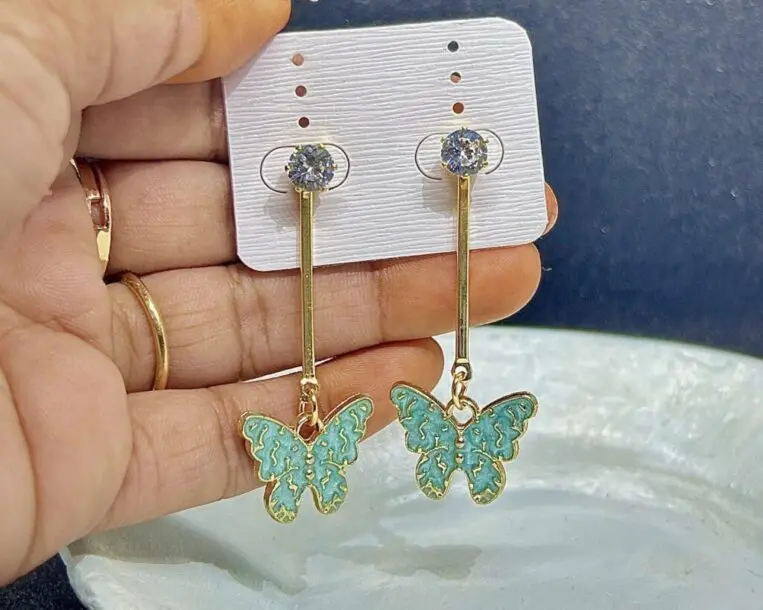 A pair of drop earrings with a small, golden butterfly charm with a delicate green enamel finish.
