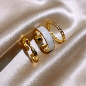 A set of three gold-plated rings with small, white details, including pearls or stones.