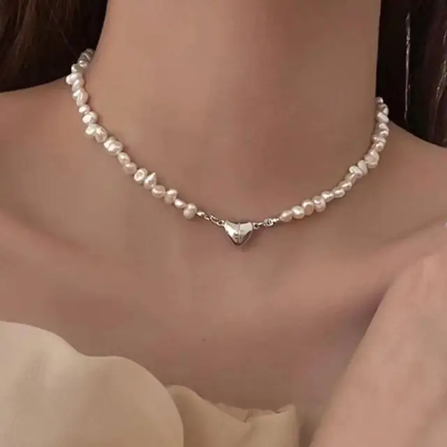 A gold-plated pendant in the shape of a heart, with a small, delicate pearl at its center.