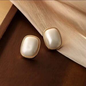 Elegant gold and pearl stud earrings on wooden and fabric surface