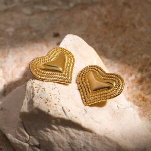 Gold heart-shaped earrings on textured white stone background.